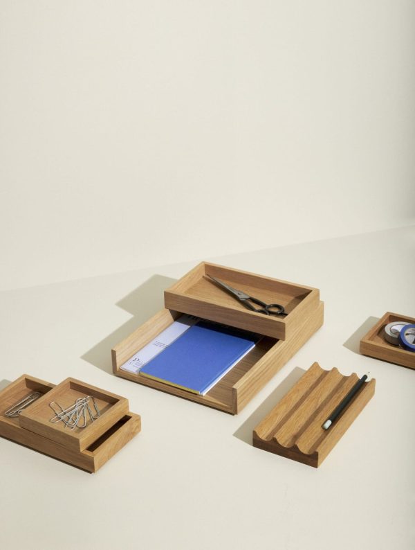 En minimalistisk kontoropsætning med elegante skrivebordsarrangører i træ. Forskellige stykker indeholder forsyninger som papir, saks, clips og en pen, pænt arrangeret på en tofarvet baggrund med accenter af designermøbler.