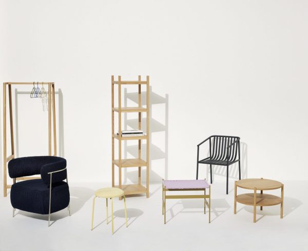 En samling af moderne designmøbler, herunder en lænestol i plys marineblå, en stol med metalramme, diverse træhylder og små taburetter, pænt arrangeret i et lyst, neutralt rum.
