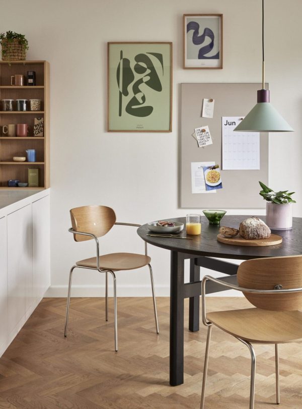 Et moderne køkken med et rundt, sort spisebord med to træstole, en hvid bordplade og indbyggede hylder. Der er minimalistisk kunst på væggene fra Tomorrowsdesign og en
