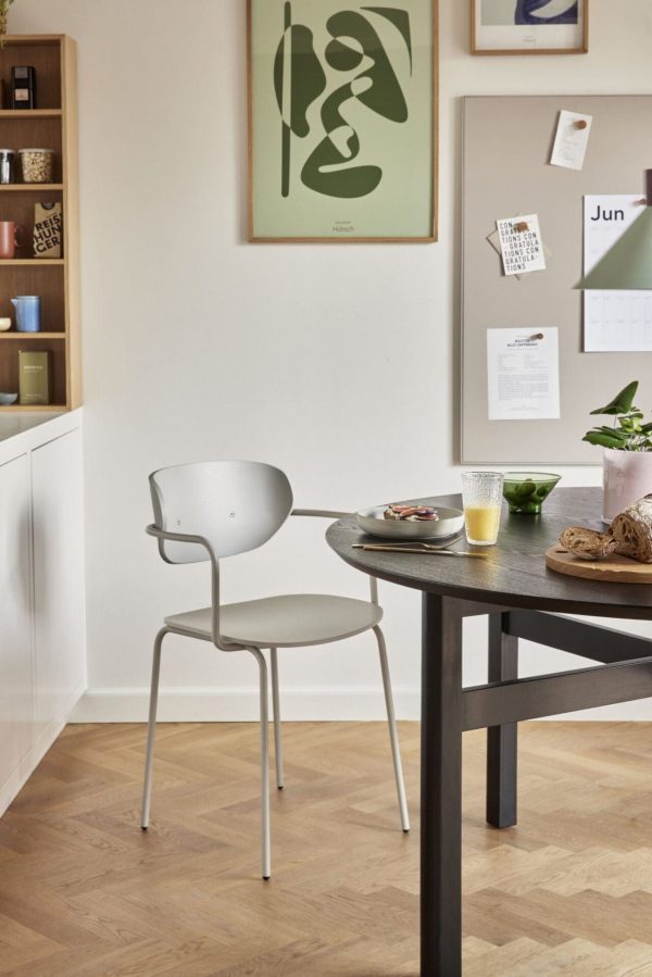 En moderne spiseplads med et sort bord med en grå stol. Rummet har hvide skabe, en korkplade og grøn og hvid vægkunst. Et lille måltid og drikkevarer er på designermøblerne