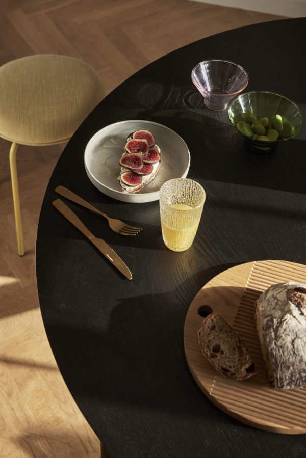 En moderne spisestue på et sort cirkulært bord med en tallerken med figner, et glas juice, oliven i en skål og et designermøbelfad med brød, oplyst af
