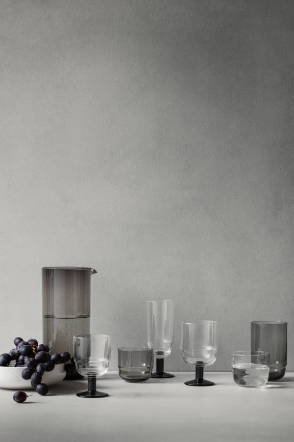 Et minimalistisk arrangement på en grå kulisse med en klynge af mørke druer, en fransk presse og et udvalg af forskelligt formede og størrelser BROSTE COPENHAGEN - 'Nordic Bistro' Champagneglas.