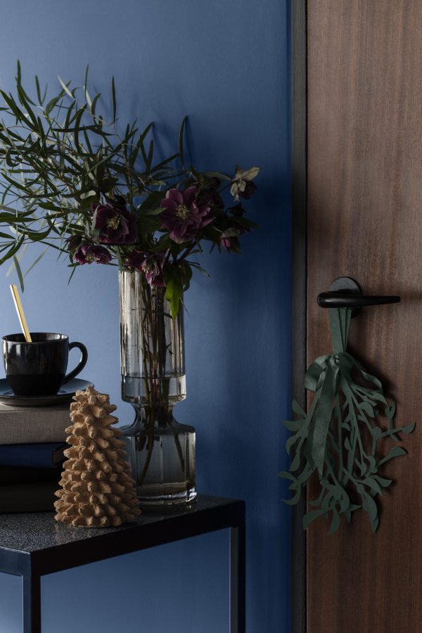 En vase med blomster og en fyrrekogle på et møblerbord.