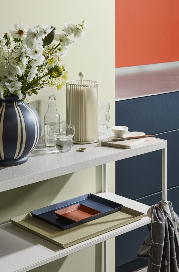Et stilfuldt boligdesign med en farverig geometrisk væg med et slankt konsolbord med en blå vase med hvide blomster, en cremefarvet kaffemaskine og minimalistisk køkkentilbehør.