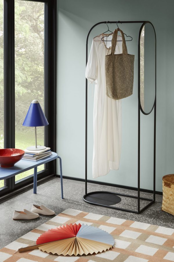Et TomorrowsDesign-stil med et minimalistisk tøjstativ med en hvid kjole og en mulepose. En blå lampe, dekorative bøger og en foldet papirventilator pryder rummet. EN