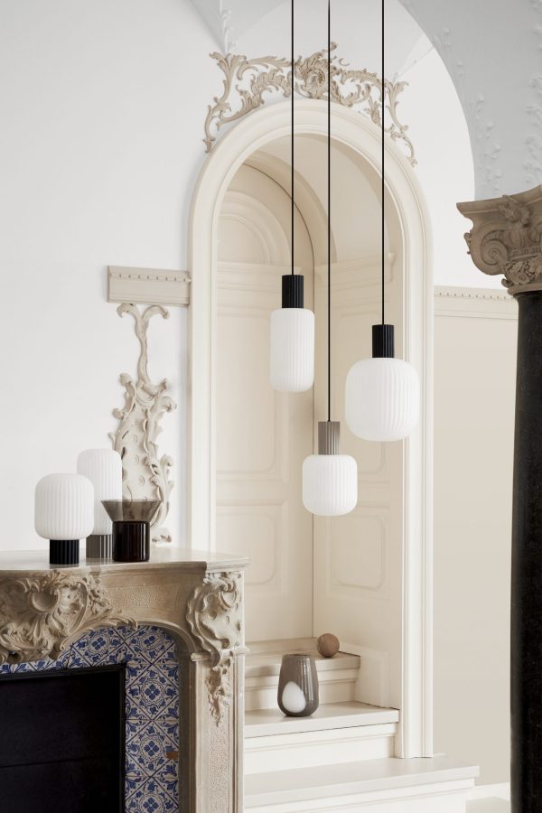 Elegant interiør med udsmykket hvid buegang, med en serie af moderne hvide pendellamper, der hænger over en elegant sort pejsekappe dekoreret med matchende hvide lamper.