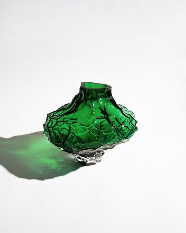En tekstureret grøn glasvase med Tomorrows-design sidder på en hvid overflade og kaster en levende grøn skygge.