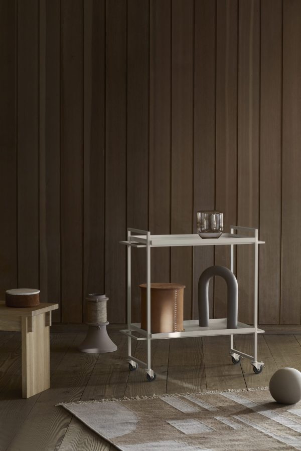 Et minimalistisk boliginteriør med en KRISTINA DAM - Opal Vase Lille med genstande på, ved siden af en træskammel og et lille sidebord. rummet har træpaneler og et tekstureret tæppe.