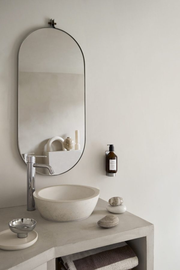 En minimalistisk badeværelsesdisk med en rektangulær vask, et monteret KRISTINA DAM - Dowel Spejl spejl og forskellige toiletartikler, sat op mod en neutral tonet væg.