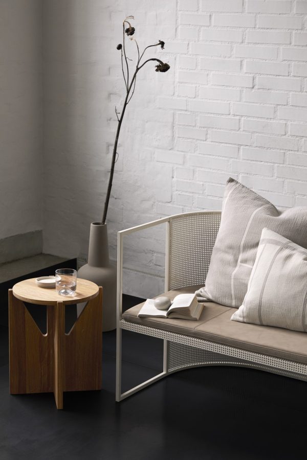 Et moderne opholdsrum med et minimalistisk design med en grå metal- og mesh-sofa med beige hynder, et lille rundt træbord med et glas vand og en åben bog på, ved siden af en høj