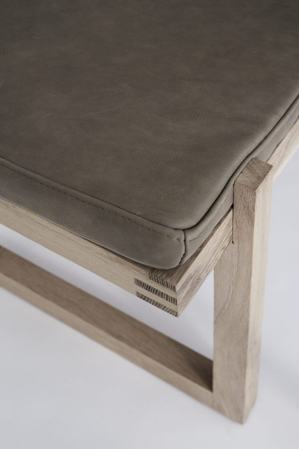 Nærbillede af en moderne bænk med en slank, grå polstret sædehynde og en let træramme med synlige snedker- og træstrukturdetaljer i banebrydende design.
