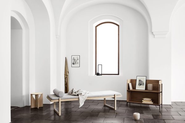 Minimalistisk interiør med hvidt buet loft, stort buet vindue der slipper lys ind og moderne designmøbler med chaiselong, lille træbord med bænk og hylder