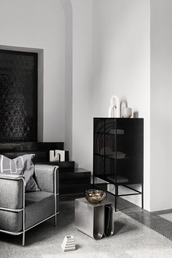 Moderne minimalistisk stue med grå sofa, sidebord med stålramme, dekorativ sort reol med vaser og abstrakt kunst på væggen. En neutral farvepalet og geometriske designs fra Tomor
