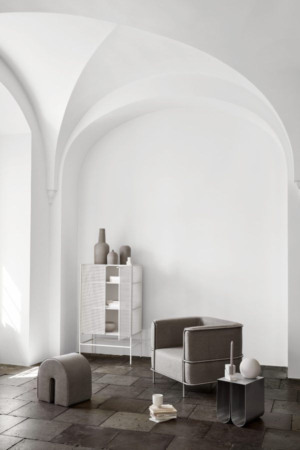 Et minimalistisk interiørdesign med et buet hvidt loft over et subtilt arrangement af møbler, inklusive en brun lænestol, en hvid reol med vaser og en grå skammel.