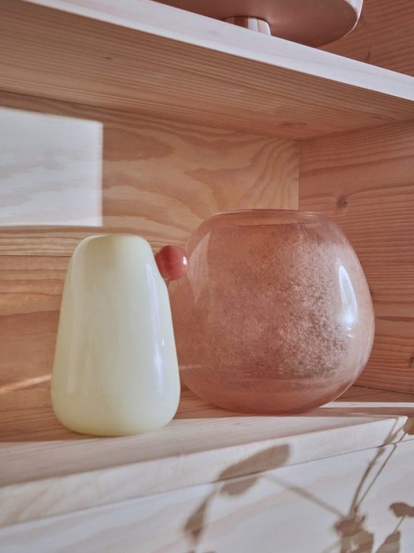 En hvid keramikvase og en rund glasvase fyldt med lyserødt Himalayasalt, begge placeret på en træhylde med blødt naturligt lys, der kaster blide skygger, og fremviser Tomorrows design-æstetik.