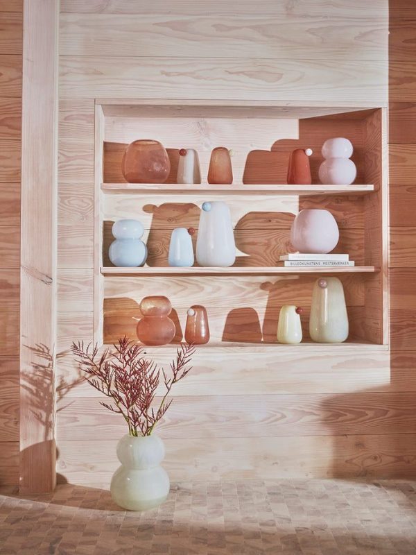 En pænt organiseret træhylde, en ægte designermøbel, der viser en samling af keramik- og glasvaser i forskellige bløde farver inklusive pink, terra cotta og lyseblå. En vase med