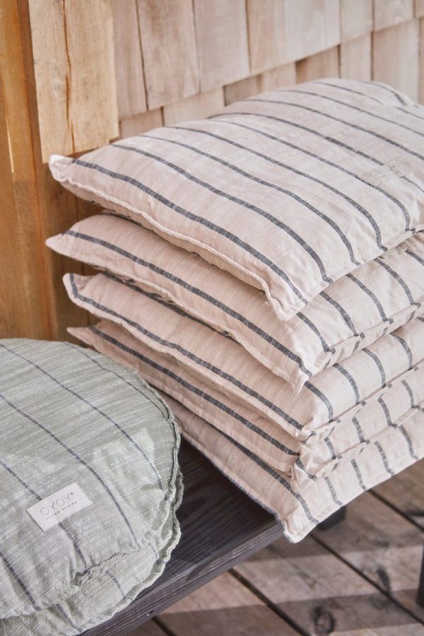 Stak af tre stribede hørpuder i naturlige toner på en træbænk, en grøn og to beige, mod en træpanelbaggrund af Tomorrowsdesign.