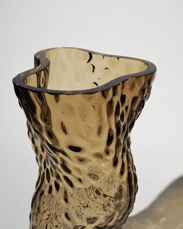 Kunstnerisk glasvase med en uregelmæssig kant og en struktureret overflade med et plettet, gennemskinnelig beige mønster. Designet skaber et indtryk af delikat flydende og organisk form, perfekt til enhver Tomor