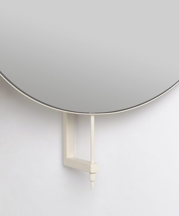 Et moderne, rundt bord med en glat, reflekterende glasplade og en unik hvid metalbund bestående af sammenlåsende rektangler, sat mod en almindelig grå baggrund af KRISTINA DAM - Rotating Spejl.