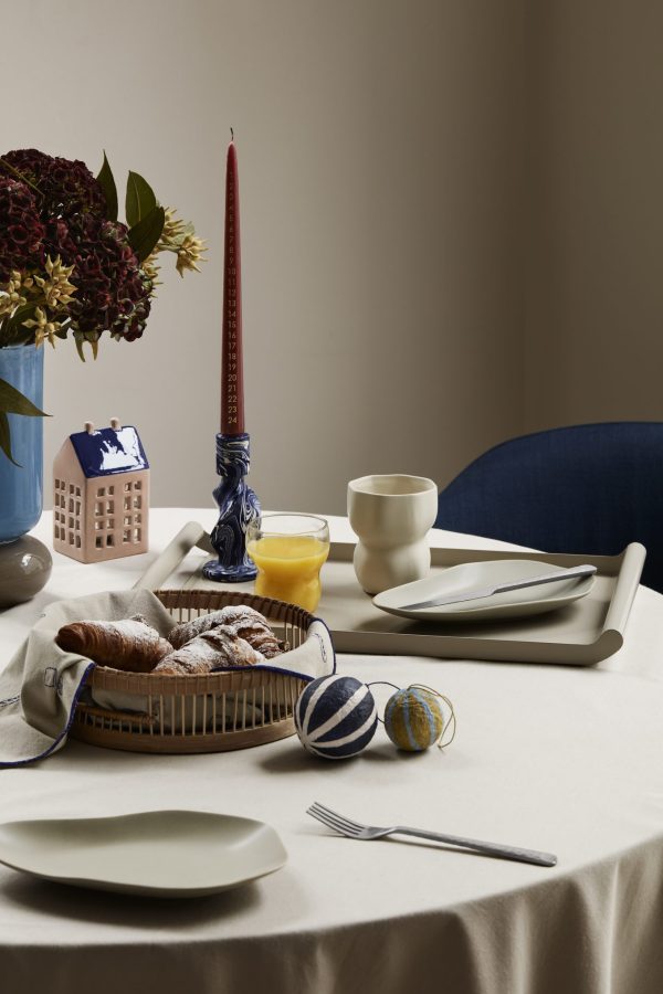 Et veloprettet morgenbord med en kurv med croissanter, keramiske tallerkener, kopper og et højt rødt lys i en blå holder, accentueret af et lille blomsterarrangement og BROSTE COPENHAGEN - 'Dorit' Vase på en neutral klud.