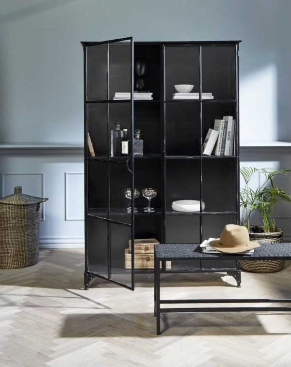 En stilfuld sort sammenklappelig bogreol fyldt med bøger, pynteting og planter i en moderne stue med sildebensparketgulv og lyseblå vægge med elegant designmøbler.