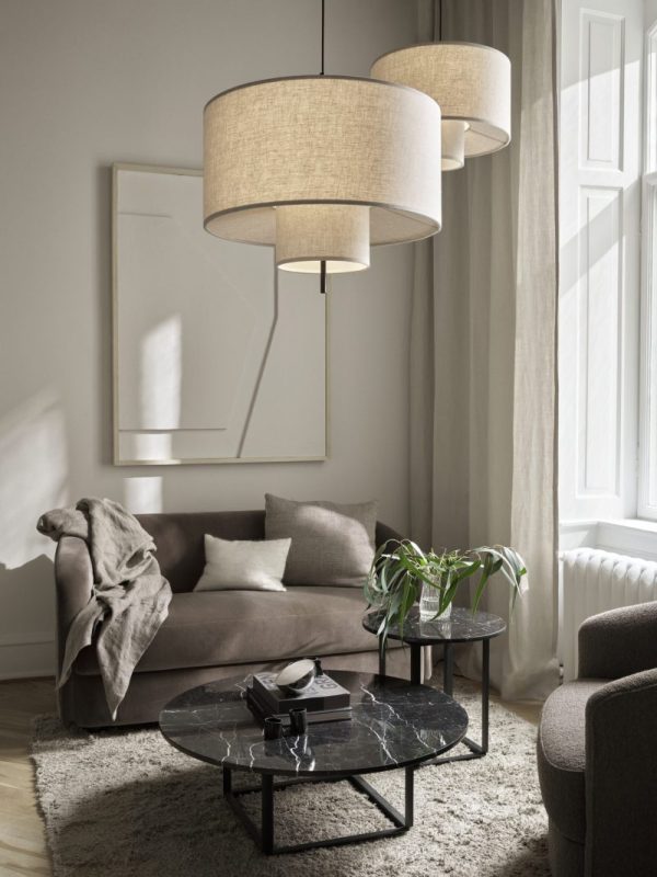 Elegant stue med beige sofa, stablet runde marmor sofaborde og store skyggefulde pendellamper. Et tæppe, stueplante og bøger dekorerer også rummet med skandinaviske møbler.