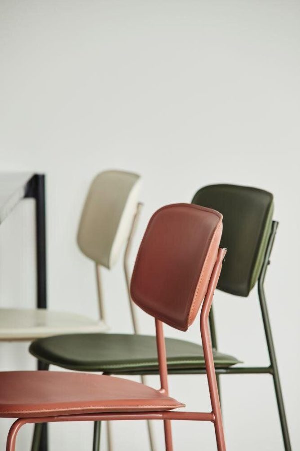 Tre moderne stole med slankt design, stablet let overlappende i nuancer af rød, hvid og grøn, sat mod en dæmpet hvid baggrund, der inkarnerer essensen af TomorrowsDesign.