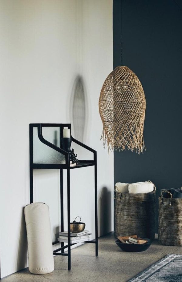 Et moderne hjørne af et værelse med en minimalistisk grå væg, en sort metalhylde med forskellige ting, en hængende vævet lampe og tre designmøbler-kurve på gulvet. En subtil teksturkontrast er tydelig i indretningen.