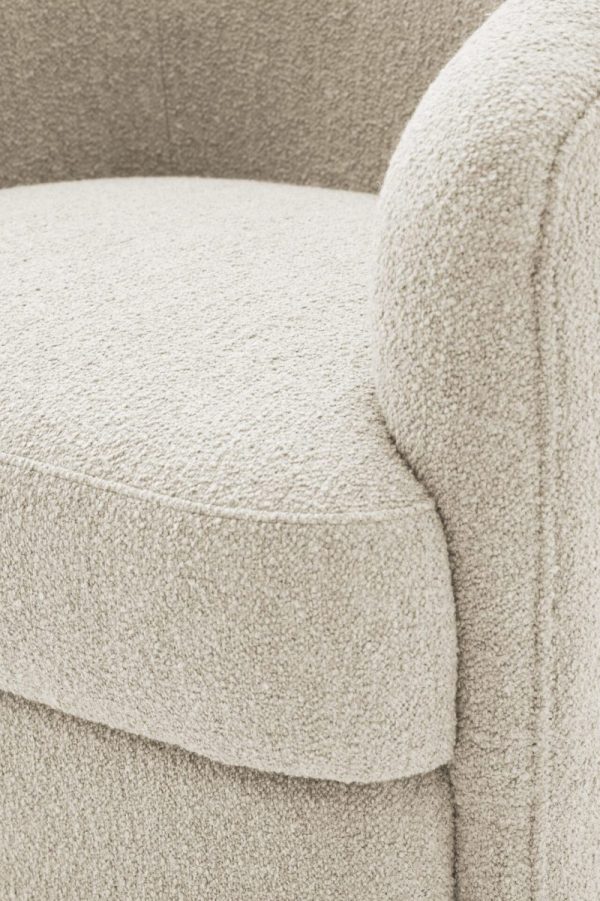 Nærbillede af en beige tekstureret lænestol med fokus på dens hynde og armlæn, der viser detaljeret stoftekstur i et monokromt farveskema, der fremhæver dets udsøgte design.