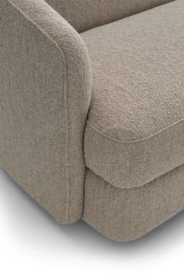 Nærbillede af en beige stofsofa, der viser detaljeret tekstur af dens polstring og syninger på det tykke polstrede armlæn, ideel til designmøbler-entusiaster. Baggrunden er en almindelig lys farve.