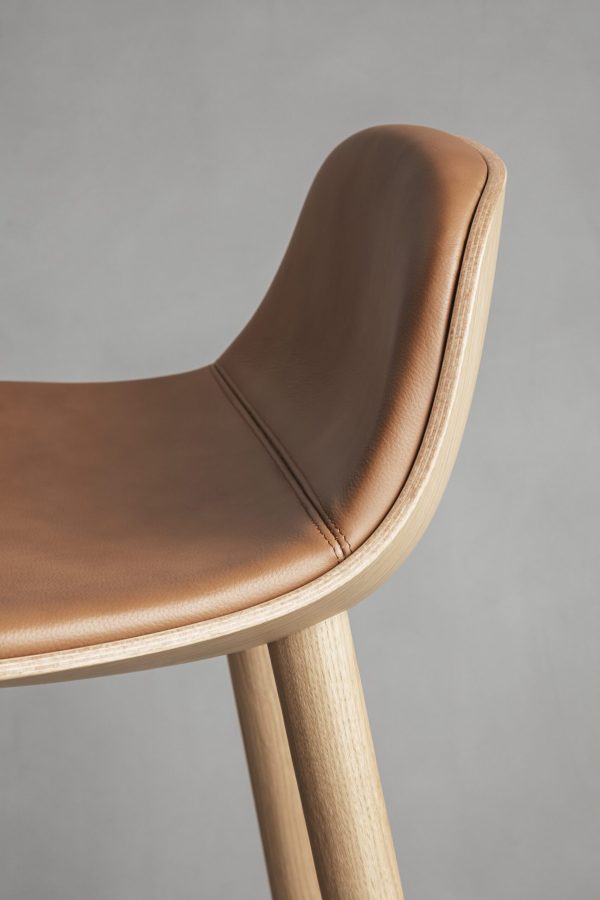 Nærbillede af en moderne stol med et glat, lysebrunt lædersæde og ryglæn på en træramme, der viser detaljerede syninger og træstruktur på en grå baggrund. Dette stykke er perfekt til moderne interiørdesign.
