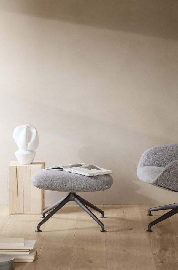 Moderne minimalistisk stue med lyst trægulv, to grå stofstole, et sidebord i træ med en hvid busteskulptur og bøger på gulvet. Væggene er i en varm beige tone.