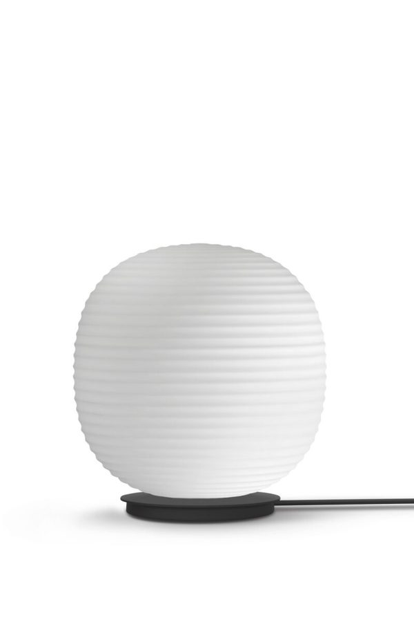 En moderne hvid NEW WORKS - Lantern Globe Bordlampe med vandrette kanter, forbundet til en strømkilde med en synlig sort ledning, stående mod en almindelig hvid baggrund.