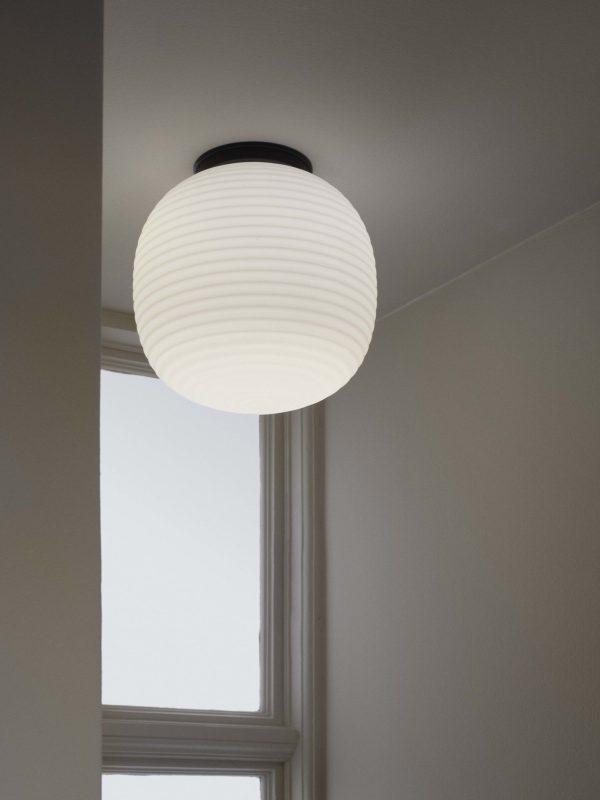 ET NYT VÆRK - Lanterne Loftslampe Ø30 med ribbet tekstur hænger fra loftet i et rum med lysegrå vægge og et højt, smalt vindue. vinduet giver naturligt lys, der blødt oplyser rummet.