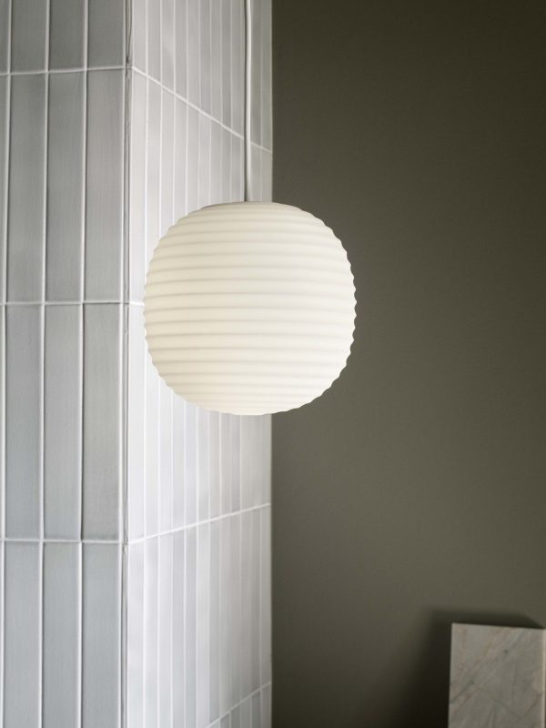 Et minimalistisk billede, der viser en rund, ribbet lampe monteret på en grå væg, delvist oplysende hvide gardiner og et glimt af en marmoroverflade af TomorrowsDesign.