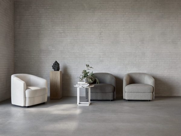 En minimalistisk stue med to grå sofaer og en hvid lænestol, med et lille bord med en plante og en skulptur på en piedestal mod en hvid murstensvæg. Oplev TomorrowsDesignelementer i dette rum.