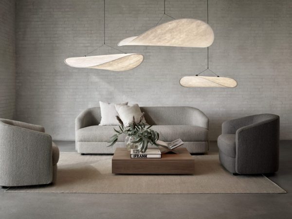 En stilfuld moderne stue med en grå sofa med matchende lænestole, et NEW WORKS - Mass Wide Sofabord og karakteristiske aflange pendellamper. neutrale toner og teksturer fylder rummet.