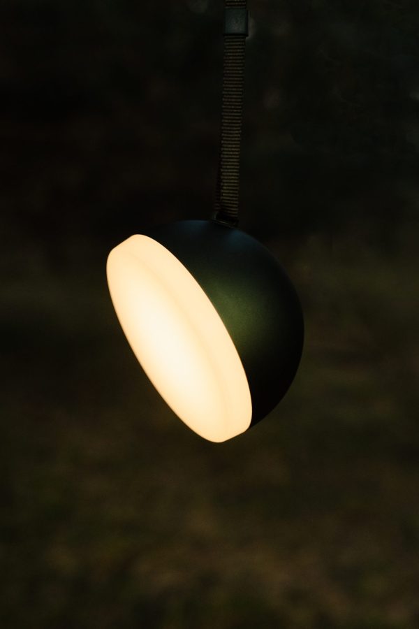 En hængende Sphere Adventure Lampe udsender en blød, varm glød mod en mørk baggrund, dens ovale form og glatte sorte ydre ophængt af en mørk rem.