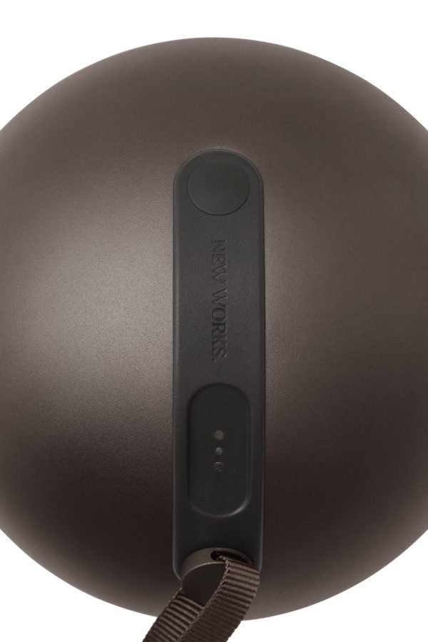 Nærbillede af en matbrun Sphere Adventure Lampe med en rem og etiketten "keywords" på en rund knaplignende funktion. Enheden har tre små synlige indikatorlamper.