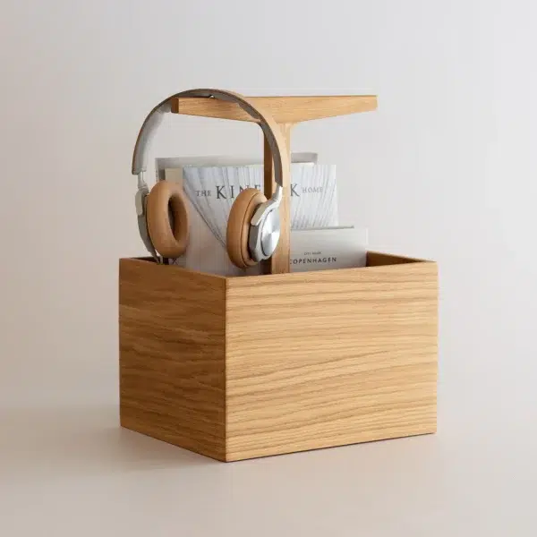 En trææske fra TomorrowsDesign, der pænt opbevarer et par høretelefoner hængende på siden og to bøger indeni, mod en almindelig lys baggrund.