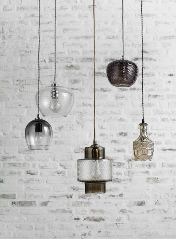 Fem unikke pendellamper, der hænger op ad en tekstureret hvid murstensvæg, hver med en forskellig form og møbeldesign, med klart og tonet glas sammen med metalaccenter.