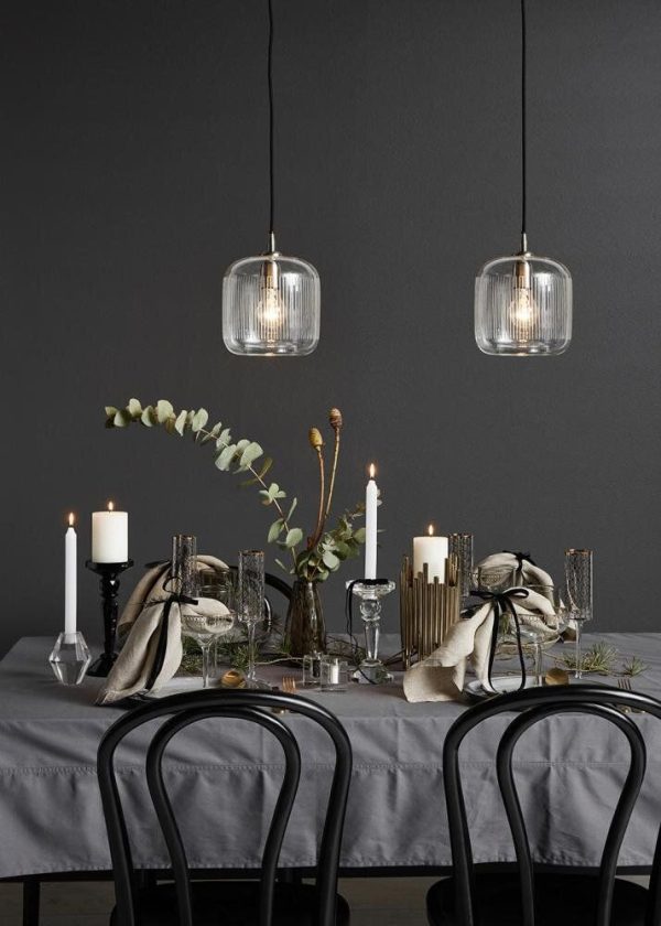 Elegant spisestue med et mørkt bord med sorte stole, dekoreret med stearinlys, glasvarer og grønt. To moderne pendellamper fra TomorrowsDesign hænger ovenover og kaster et blødt skær på bordet.