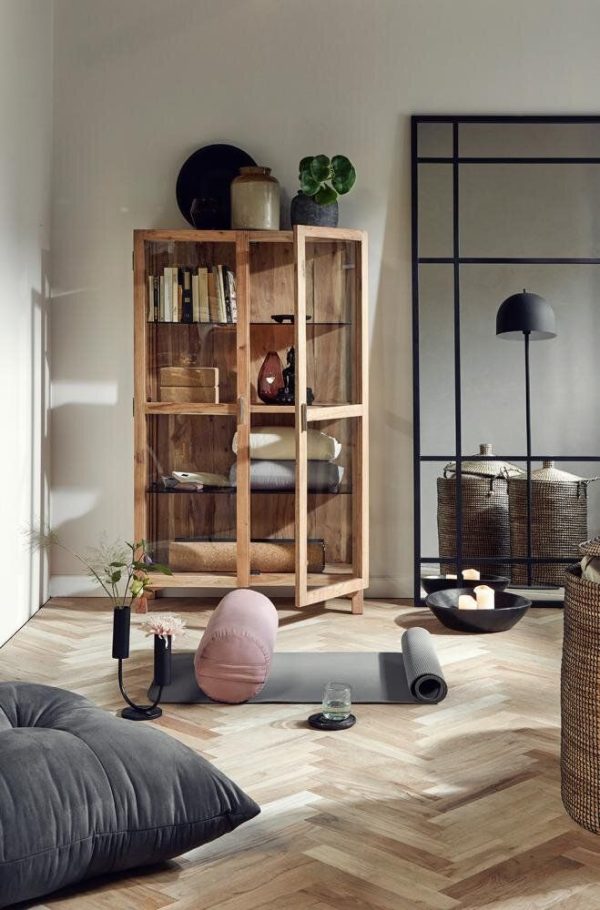 Moderne stue med bogreol i træ fyldt med bøger og pynteting, en yogamåtte rullet ud på sildebensgulvet, frodige indendørs planter og hyggelige gulvpuder under blødt naturligt lys fra TomorrowsDesign.