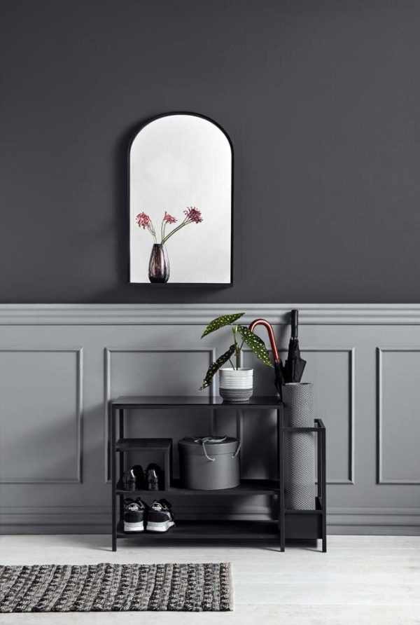 En moderne gang med en mørkegrå væg med en stiliseret sort metalhylde fra TomorrowsDesign med sko, tasker og en potteplante. Ovenfor er et spejl, der afspejler en vase med blomster.