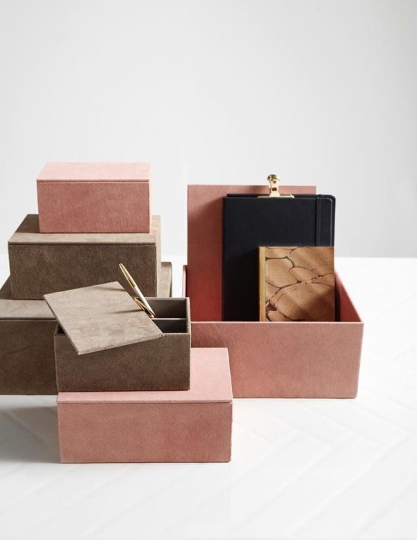 En samling af åbne og lukkede ruskindsæsker i nuancer af pink og brun, pænt arrangeret i henhold til TomorrowsDesign, med en æske indeholdende en bog og en metallisk pen.