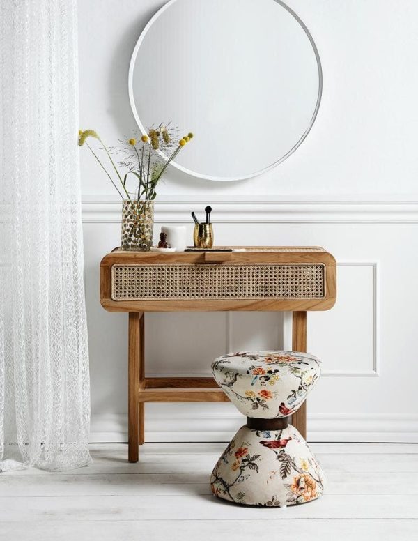 Et moderne interiør med et konsolbord af træ med front i rattan under et stort rundt spejl. En blomstret polstret skammel sidder i nærheden, og en vase med vilde blomster er placeret på bordet. Hvide vægge og gennemsigtige gardiner fuldender scenen, hvilket afspejler en essens af TomorrowsDesign.