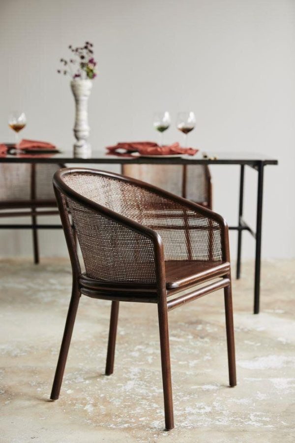Et smagfuldt dækket spisebord med en brun vævet stol i forgrunden. Bordet er prydet med fade, glas og et blomsterarrangement i baggrunden på et tekstureret gulv, alt sammen afspejler essensen af TomorrowsDesign.
