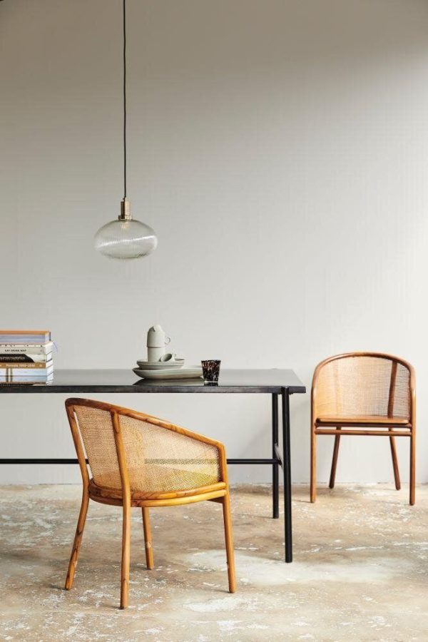 En minimalistisk spiseplads med et sort bord og to kurvestole, under en hængende sølvpendel, mod en neutral væg. Bøger og en kaffekop hviler på bordet med skandinavisk designmøbler.