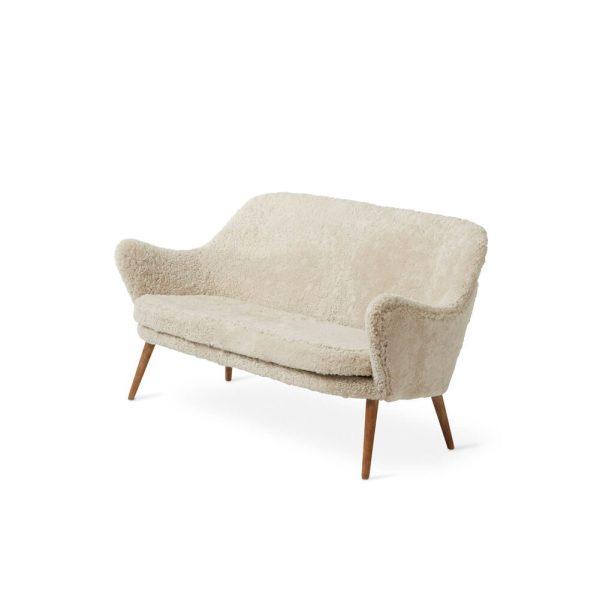 En moderne beige to-personers fåreskindssofa med buet ryglæn og sæde, stående på fire skrå træben, isoleret mod en hvid baggrund, er et perfekt eksempel på skandinavisk designmøbler.