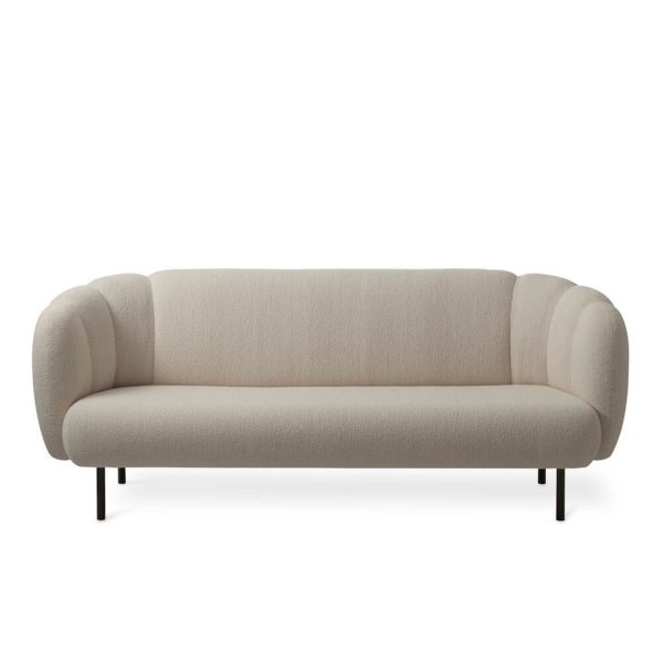 EN VARM NORDISK - Cape Sofa med et rent, minimalistisk design med en neutral beige polstring og afrundede armlæn, sat mod en almindelig hvid baggrund. Sofaen hviler på fire slanke, sorte metalben.